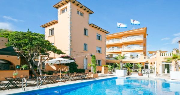 Das Van der Valk Hotel BARCAROLA ist ein 4-Sterne-Hotel im mediterranen Stil an der Costa Brava mit Balkonen mit Fahnen, einem klaren blauen Pool, Pooltischen mit Sonnenschirmen und Palmen unter einem strahlend blauen Himmel.