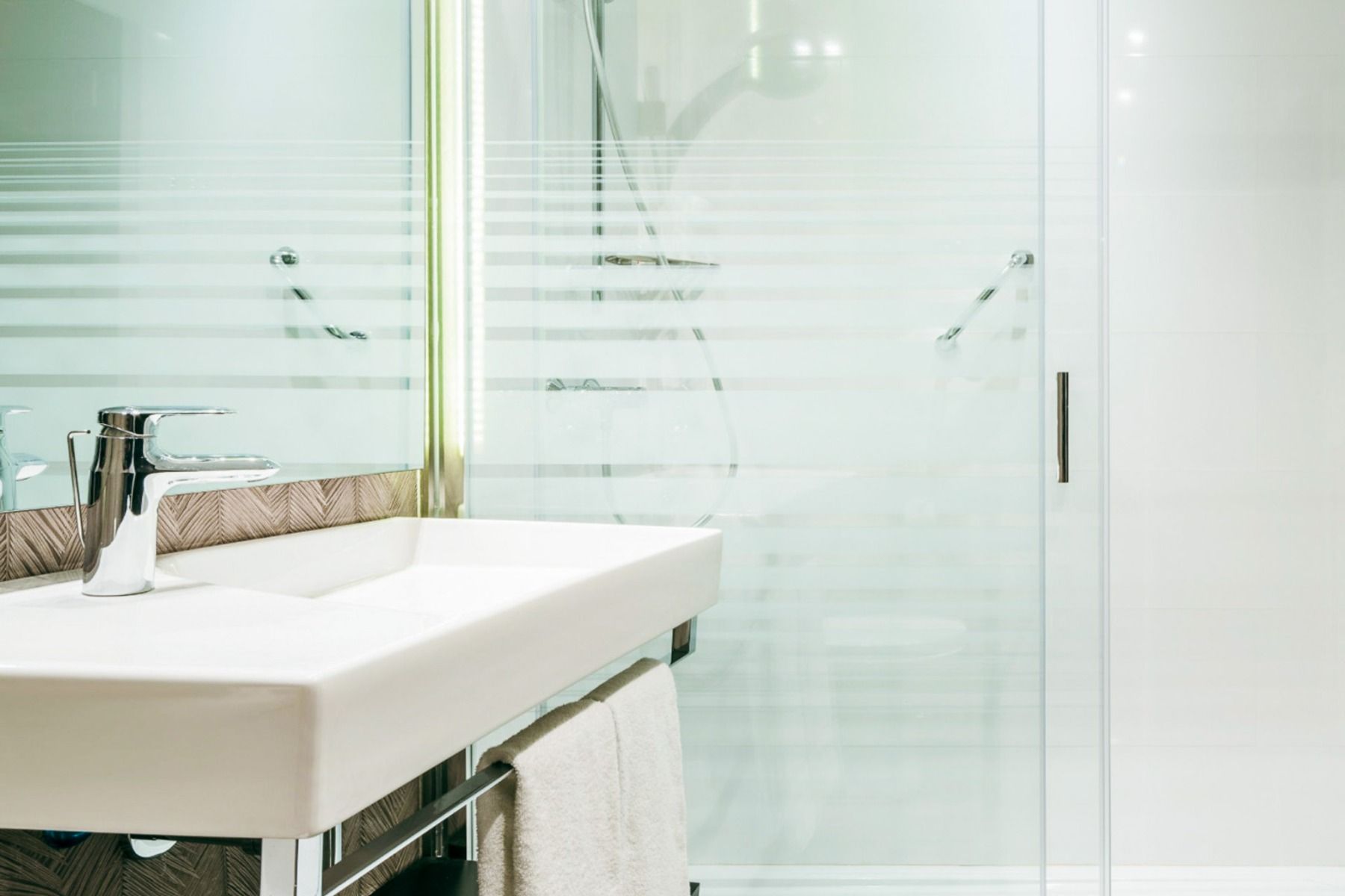 Det moderne badet på Hotel ILUNION Bel Art Barcelona har en hvit, rektangulær vask, kran i krom, håndklehenger og glassdusj med frostede striper - noe som gjenspeiler den lyse, minimalistiske stilen til Barcelonas ledende fotballtreningssteder.