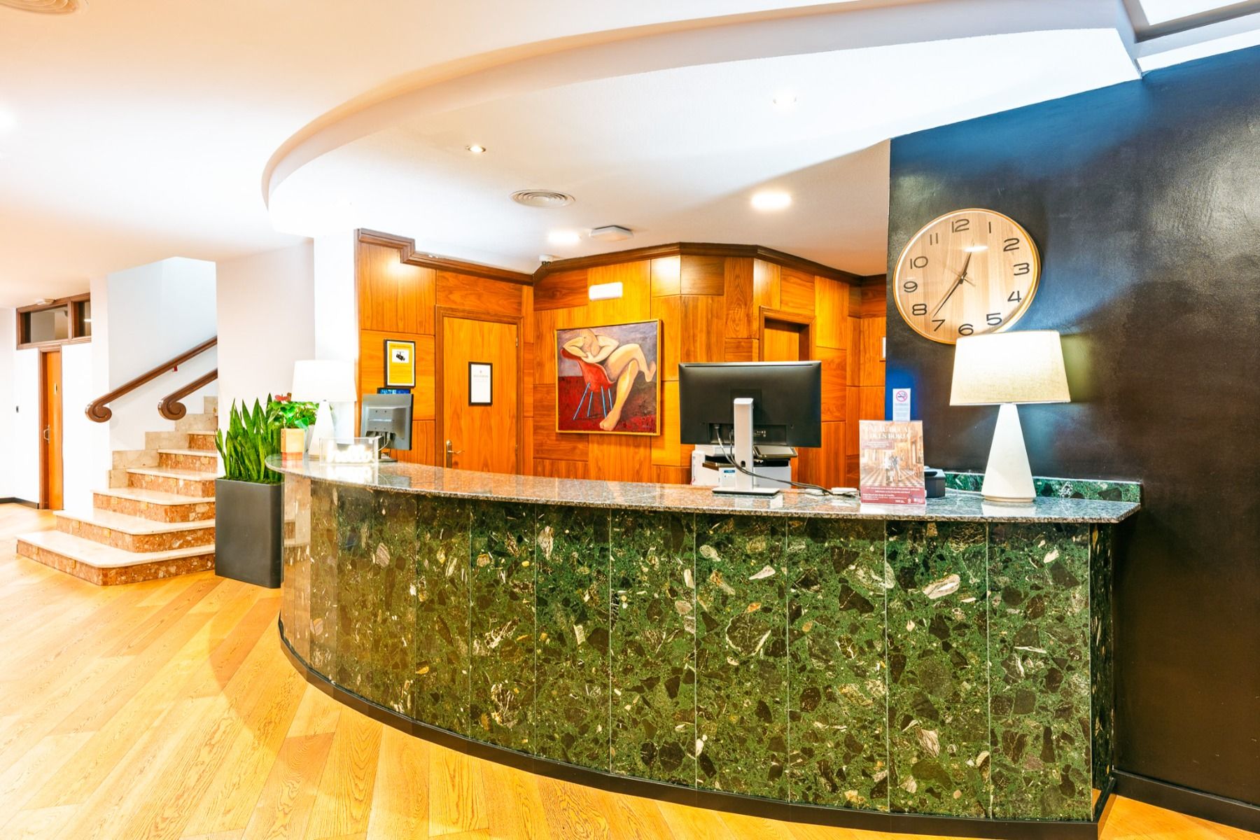 Das Hotel Borgia *** empfängt seine Gäste mit einer auffälligen, geschwungenen Rezeptionstheke aus grünem Marmor, die mit einem Computermonitor, einer Lampe und einer Wanduhr ausgestattet ist. Warme Holzvertäfelungen, raffinierte Kunstwerke und mit üppige