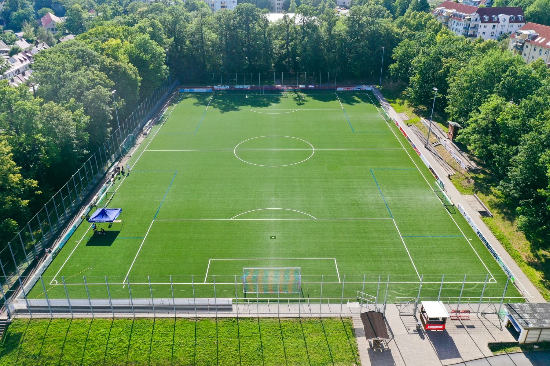 Luftaufnahme eines leeren Fußballplatzes im Freien, umgeben von Bäumen und Gebäuden, mit einem Tor an jedem Ende und einem blauen Zelt auf der linken Seite des Platzes – ideal für ein Fußballtrainingslager in der Nähe des Hotels Dorotheenhof, wo historisc