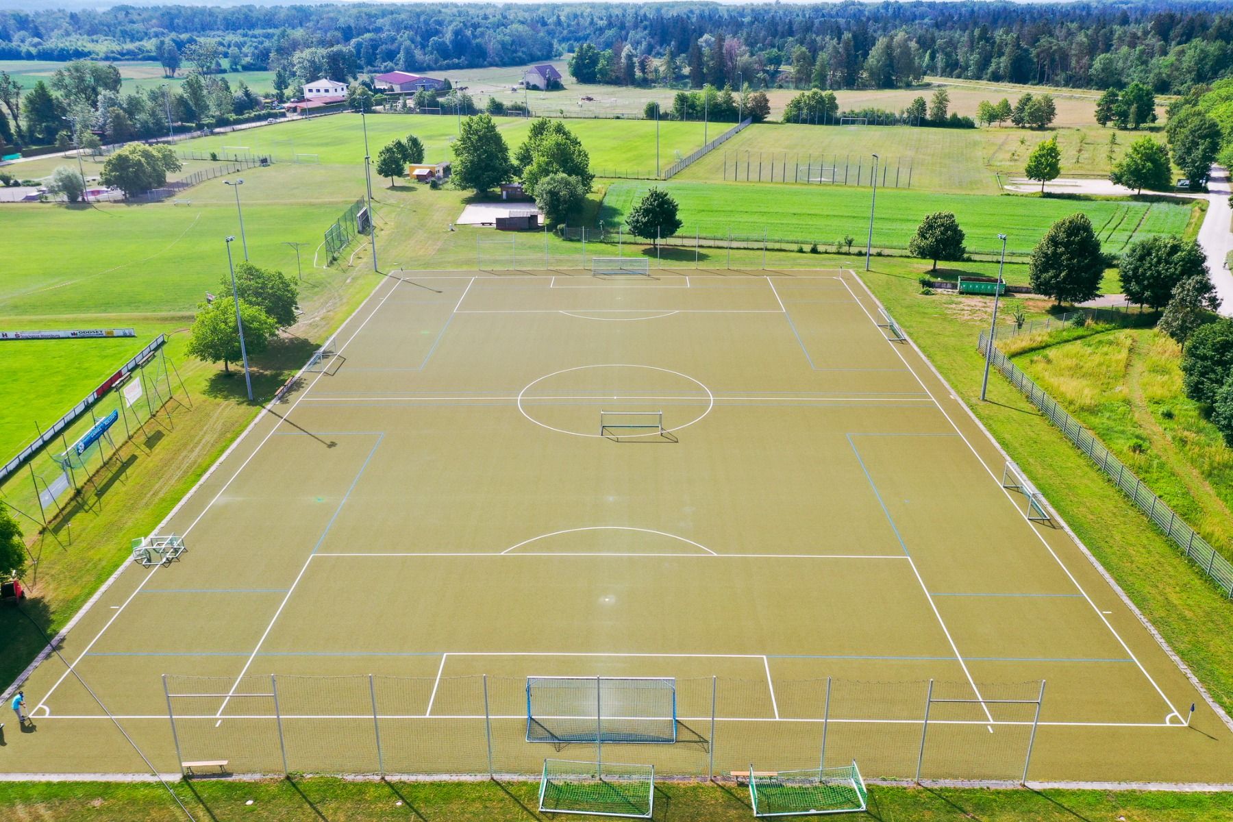 Luftaufnahme eines leeren Fußballplatzes im Freien im Sportpark Moosburg, umgeben von viel Grün und in der Nähe des Hotels Drei Rosen – ideal für ein Fußballtrainingslager bei strahlendem Sonnenschein.