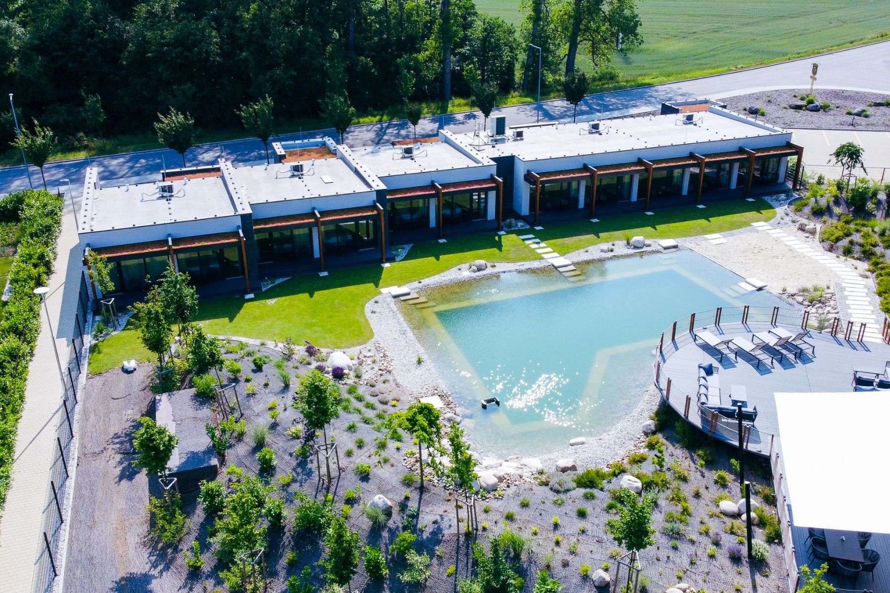 Luftaufnahme des Hotels Jagdfestung, eines modernen Gebäudes mit Flachdach, das über einen Teich, einen Landschaftsgarten und einen Terrassenbereich im Freien verfügt und von üppigem Grün und Bäumen umgeben ist – in idealer Lage direkt neben einem weitläu