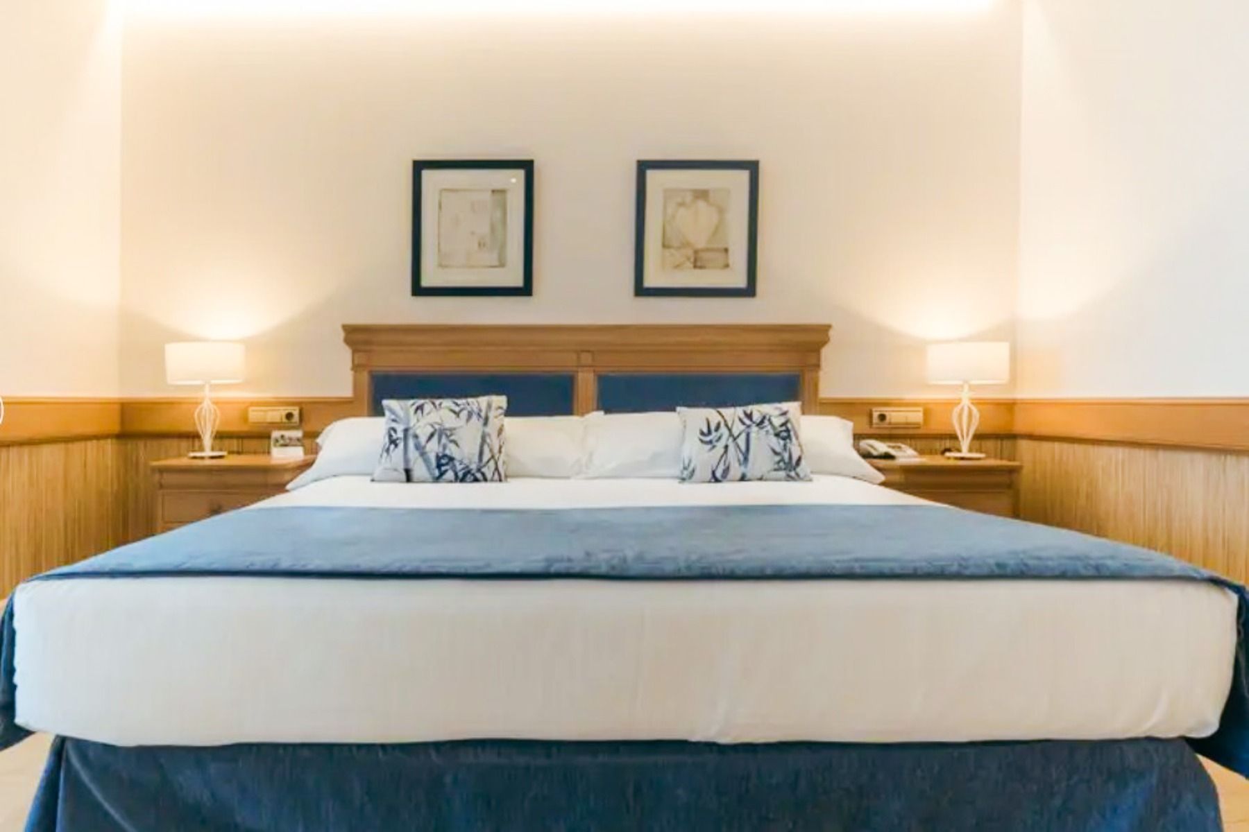 Im Hotel SH Villa Gadea*, einer beliebten Unterkunft für Fußballmannschaften während ihrer Trainingslager in Altea, steht ein ordentlich gemachtes Bett mit blau-weißer Bettwäsche zwischen zwei Nachttischen aus Holz, über dem zwei gerahmte Bilder hängen.