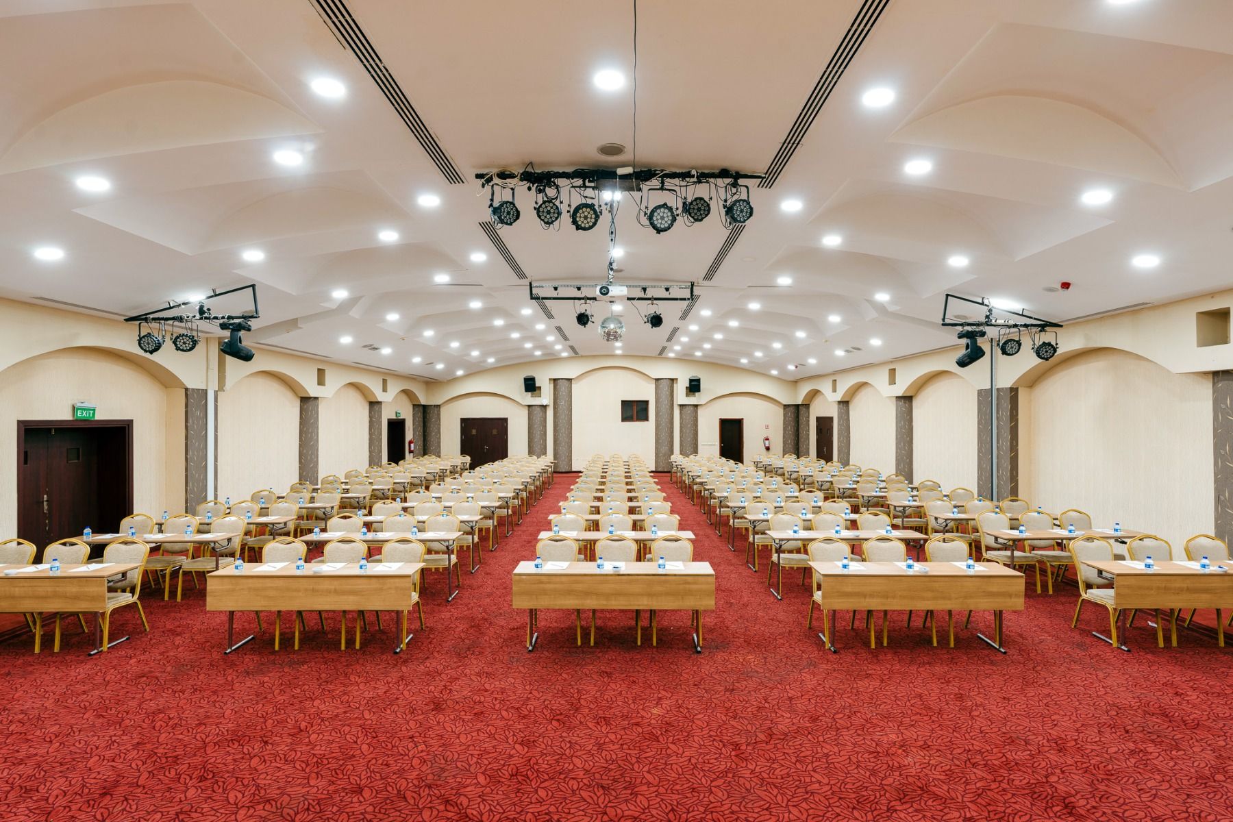 Ein geräumiger, heller Konferenzraum mit ordentlich angeordneten Holztischen und Stühlen - perfekt für das Fußballtrainingslager Türkei. Jeder Tisch ist mit Notizblöcken und Wasserflaschen ausgestattet, genau wie im Hotel Limak Arcadia.