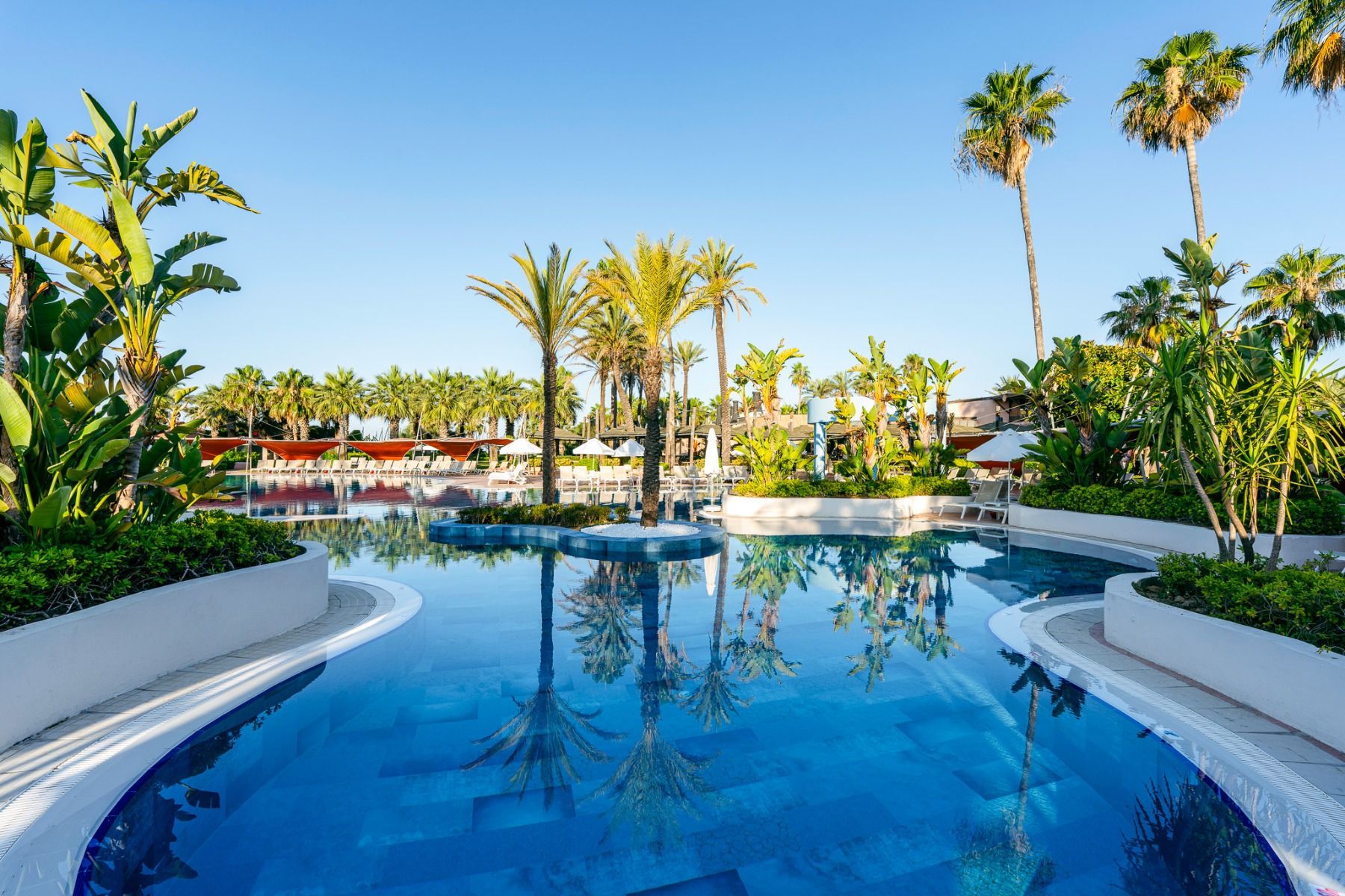 Der luxuriöse Außenpool des Hotels Limak Arcadia ist von Palmen und üppigem Grün umgeben und mit Liegestühlen und Sonnenschirmen ausgestattet - ideal zum Entspannen während eines Fußballtrainingslagers in der Türkei.