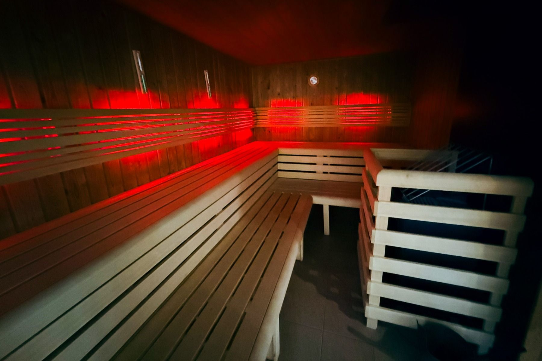 Die moderne Holzsauna von Marveld Recreatie ist mit hellen Holzbänken, roter Akzentbeleuchtung und einem Ofen mit Sicherheitsvorrichtung ausgestattet - ein einladender, schummriger Rückzugsort in den Ferienpark-Bungalows. Der Raum ist leer.