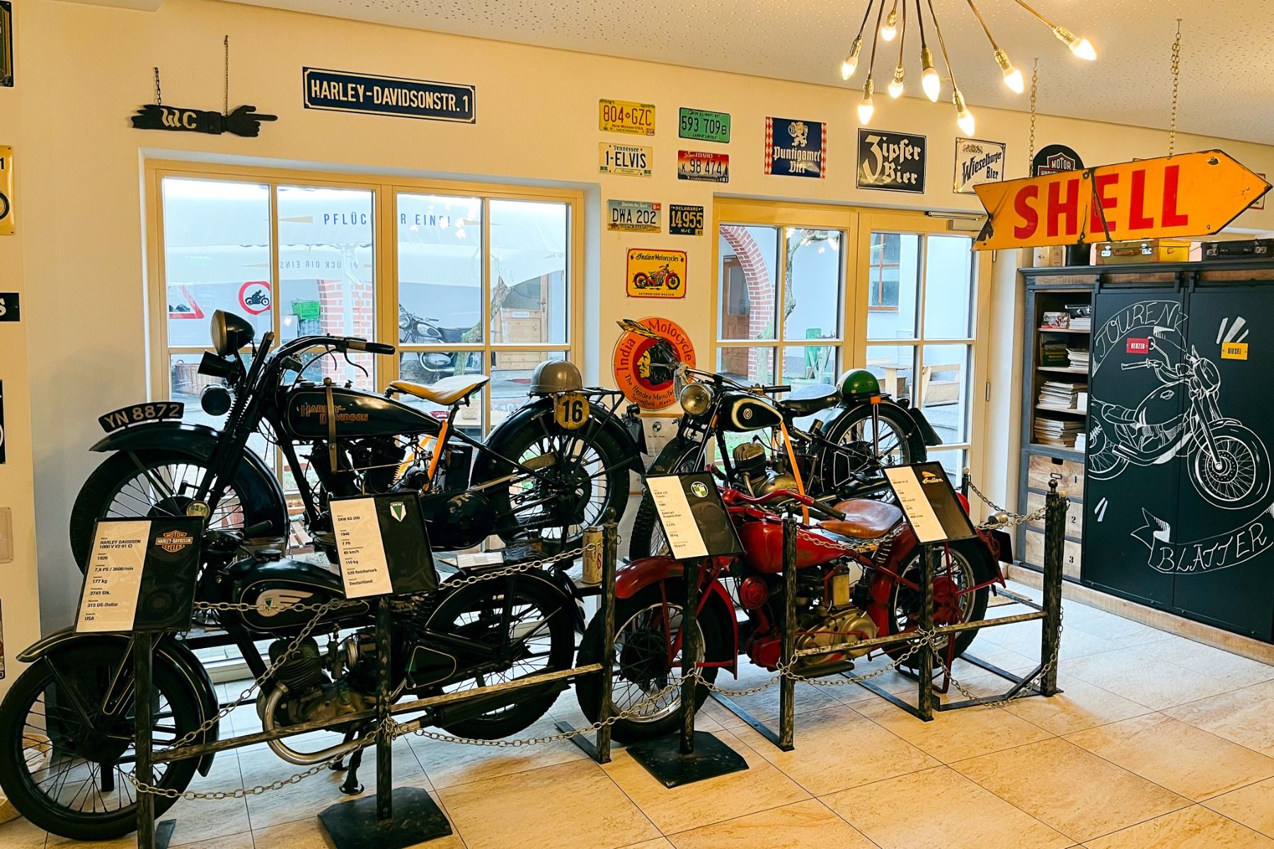 Das Perbersdorfer Heuriger - Hotel in Neuhofen an der Ybbs verfügt über eine Indoor-Oldtimer-Motorradausstellung, umgeben von Retro-Shell- und Harley-Davidson-Schildern, Seilabsperrungen, Fenstern und dekorativer Wandkunst in diesem familiengeführten Betr