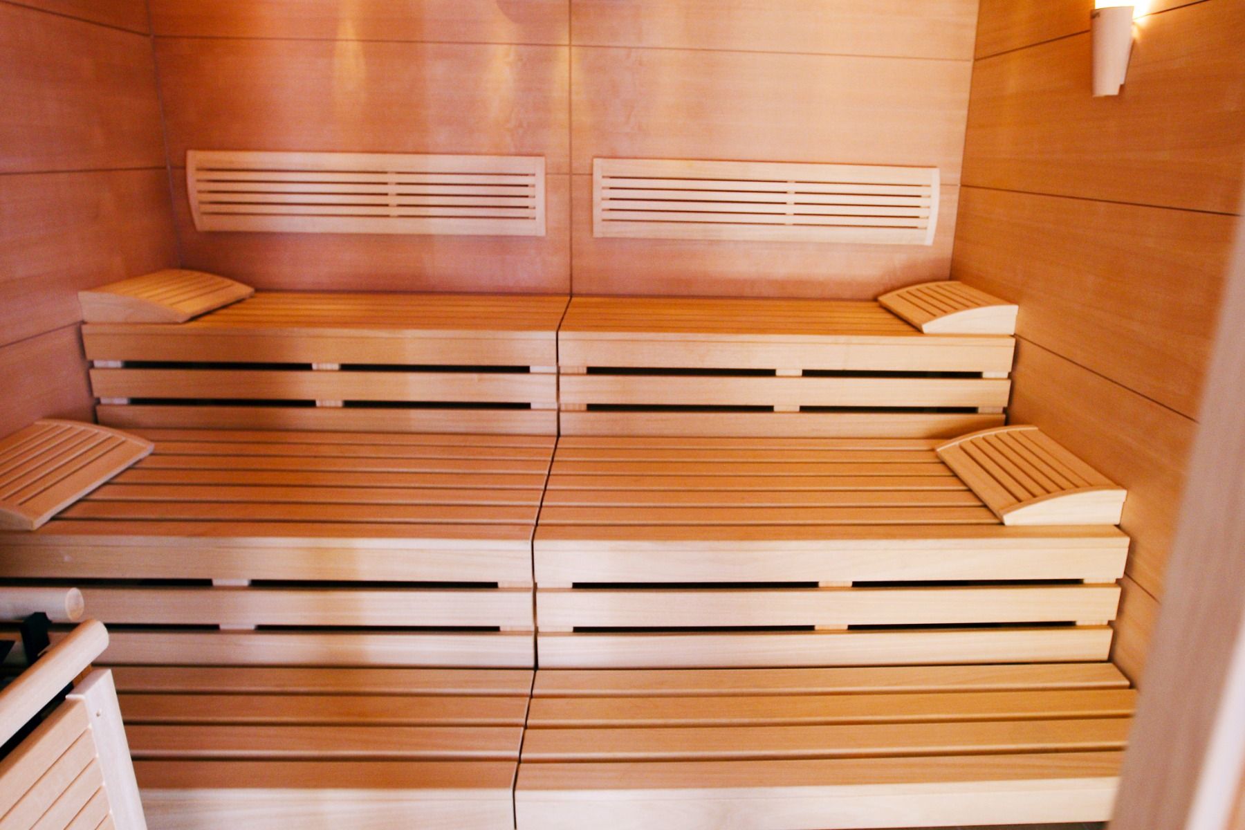 Innenraum einer modernen Holzsauna im Perbersdorfer Heurigen - Hotel mit zweistufigen Sitzbänken, Holzrückenlehnen und warmer Wandbeleuchtung, die eine saubere und entspannende Atmosphäre in diesem familiengeführten Hotel schaffen.
