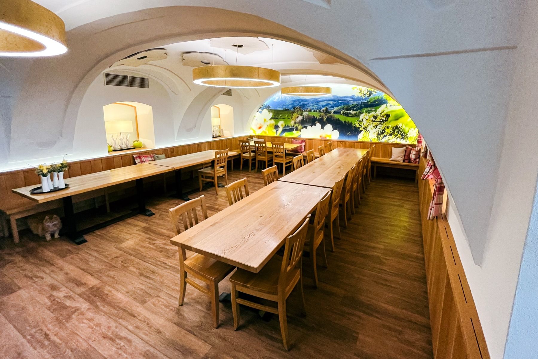 Das Perbersdorfer Heuriger - Hotel in Neuhofen an der Ybbs bietet einen modernen, familiengeführten Speiseraum mit Holz-Tischen und -Stühlen, gewölbten weißen Decken, Holzboden, warmem Licht sowie Landschaftsmalerei und Pflanzen für wohnliches Ambiente.