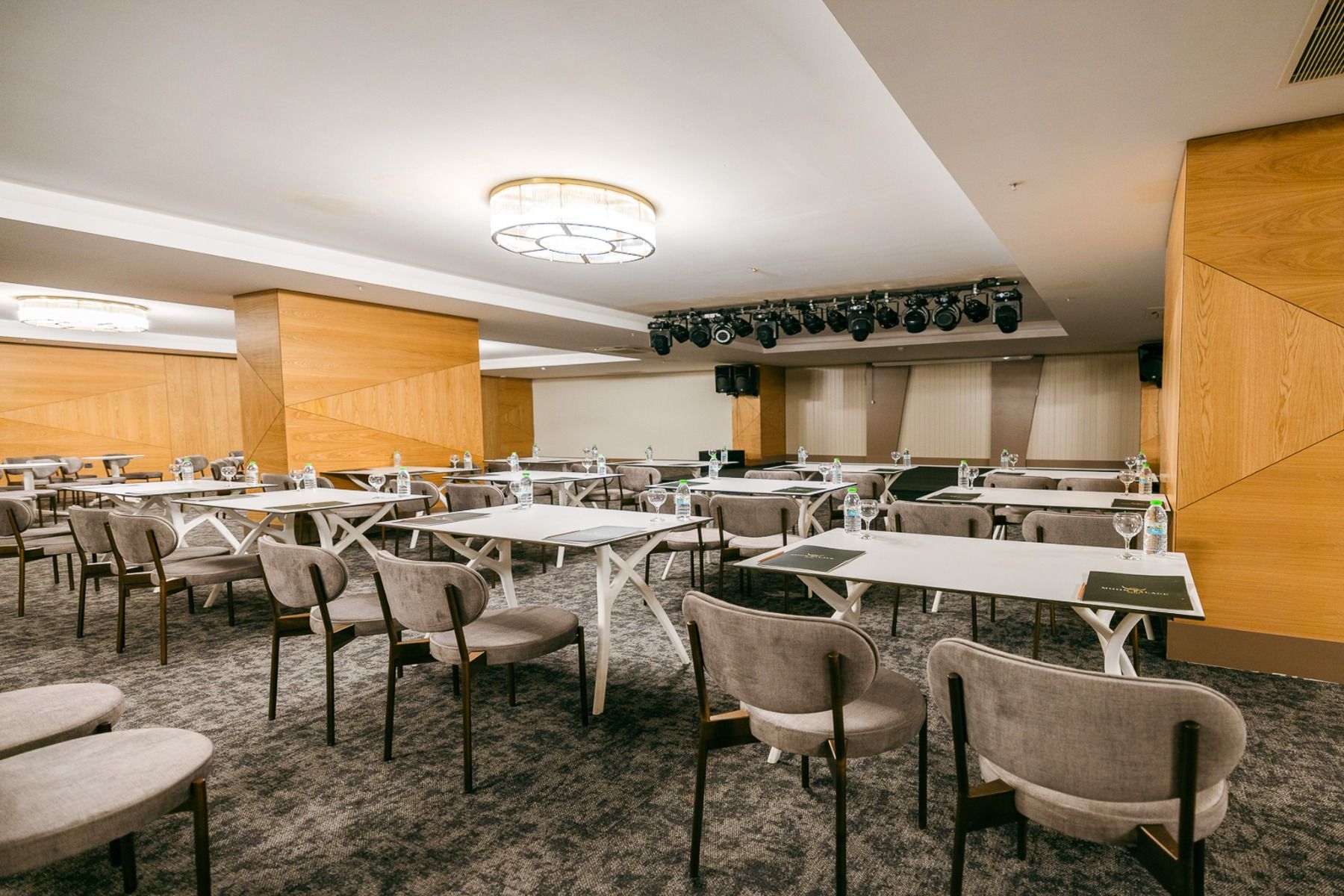 Der Side Moon Palace verfügt über einen modernen Konferenzraum mit Tisch- und Stuhlreihen, Wasserflaschen auf jedem Tisch, Deckenbeleuchtung sowie einem Bühnenbereich, der durch Scheinwerfer und Vorhänge im Hintergrund hervorgehoben wird.