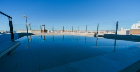 Außenansicht des Hotels Gaudea in Santa Pola mit großen Glasfenstern, die den Blick auf eine moderne, warm beleuchtete Lobby mit einem Sitzbereich freigeben. Der Name des Hotels und die vier Sterne sind über dem Eingang gut sichtbar angebracht.