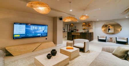 Außenansicht des Hotels Gaudea in Santa Pola mit großen Glasfenstern, die den Blick auf eine moderne, warm beleuchtete Lobby mit einem Sitzbereich freigeben. Der Name des Hotels und die vier Sterne sind über dem Eingang gut sichtbar angebracht.