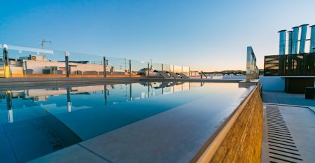 Außenansicht des Hotels Gaudea in Santa Pola mit großen Glasfenstern, die den Blick auf eine moderne, warm beleuchtete Lobby mit einem Sitzbereich freigeben. Der Name des Hotels und die vier Sterne sind über dem Eingang gut sichtbar angebracht.