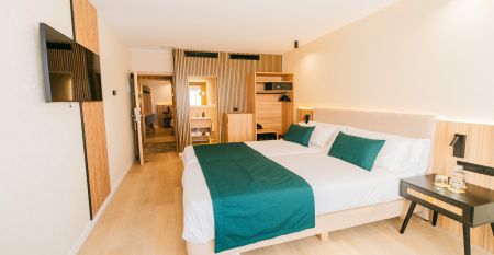 Außenansicht des Hotels Gaudea in Santa Pola mit großen Glasfenstern, die den Blick auf eine moderne, warm beleuchtete Lobby mit einem Sitzbereich freigeben. Der Name des Hotels und die vier Sterne sind über dem Eingang gut sichtbar angebracht.