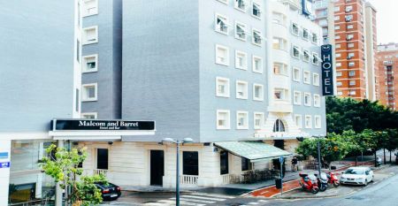 Das moderne, hellgraue Hotel Malcom & Barret Valencia*** besticht durch ein gro&szlig;es HOTEL-Schild, vor dem Motorroller und ein Auto geparkt sind &ndash; ein einladender Ort f&uuml;r die Fu&szlig;ballmannschaften aus Valencia w&auml;hrend ihres Trainingslagers.