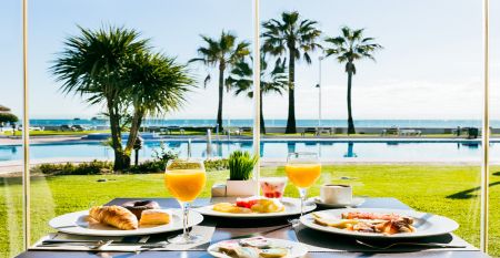 Ein hohes, gelbes Hotel Sol Guadalmar mit Balkonen blickt auf einen klaren, blauen Au&szlig;enpool, umgeben von Palmen und gr&uuml;nen Rasenfl&auml;chen unter einem sonnigen Himmel - perfekt f&uuml;r Ihren Aufenthalt in diesem zentrumsnahen 4 Sterne Hotel Malaga.