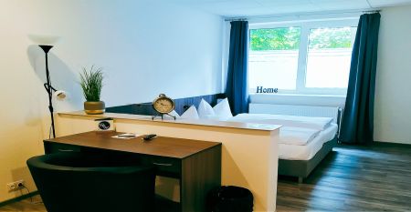 Das Hotel Stadt Mühlhausen*** besticht durch seine weiße Fassade im Industrial-Stil mit großen Fenstern. Ein Schild über dem Eingang weist auf das Hotel hin, das von Bäumen und einem bewölkten Himmel umgeben ist – ideal für Gäste des Trainingslagers oder