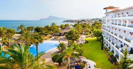 Das Hotel SH Villa Gadea* ist ein Resort an der Küste mit Meerblick, einem großen weißen Gebäude, einem Pool, Palmen und grünen Rasenflächen – ideal für Fußballmannschaften während ihres Trainingslagers in Altea unter strahlend blauem Himmel.