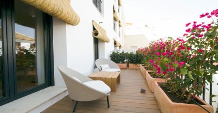 Ein Innenhof mit Palmen und Sitzgelegenheiten im Freien ist von modernen wei&szlig;en Geb&auml;uden umgeben, mit einem Hotel Zenit Sevilla-Schild - ideal f&uuml;r Fu&szlig;ball-Sportgruppen - und einem gro&szlig;en Geb&auml;ude mit der Aufschrift GOOD NIGHT auf dem Dach.