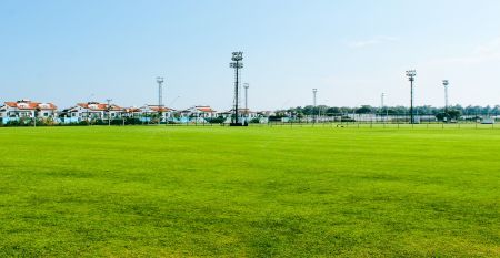 Luftaufnahme des Hotels Limak Arcadia mit Pools, Gärten, Sportplätzen und Strandkabinen - ideal für das Fußballtrainingslager Türkei - inmitten von Palmen und Bergen unter einem klaren Himmel.