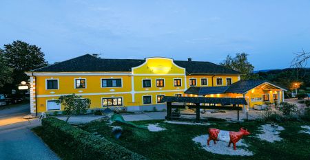 Ein leuchtend gelbes Geb&auml;ude in Neuhofen an der Ybbs mit Steg, Leiter und schwarzem Schlauchboot liegt an einem ruhigen Teich im Gr&uuml;nen - im familiengef&uuml;hrten Hotel Perbersdorfer Heuriger genie&szlig;en die Menschen diese Szene.