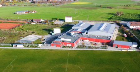 Ein pfirsichfarbenes, zweistöckiges Gebäude, der Gasthof Kapellenhof, trägt Schilder mit der Aufschrift Gästehof Kleinlandhof über der Tür und der Garage. Topfpflanzen säumen den Eingang und schaffen ein gemütliches Ambiente unter dem wolkenverhangenen Hi