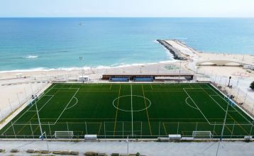 Das Hotel Barcelona Princess ragt inmitten der Hochhäuser Barcelonas nahe der Küste empor, unter einem teilweise bewölkten Himmel, unter dem sich Straßen, Autos und Bäume erstrecken – ein idealer Ort für die sportliche Vorbereitung.