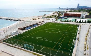 Das Hotel Barcelona Princess ragt inmitten der Hochhäuser Barcelonas nahe der Küste empor, unter einem teilweise bewölkten Himmel, unter dem sich Straßen, Autos und Bäume erstrecken – ein idealer Ort für die sportliche Vorbereitung.