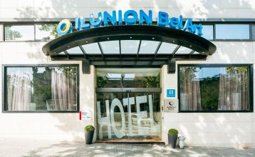 Inngangen til Hotel ILUNION Bel Art Barcelona har store glassdører, potteplanter og et skilt over den svarte markisen - perfekt for gjester som vil utforske Fußballkultur Barcelona eller besøke Trainingseinrichtungen i nærheten.