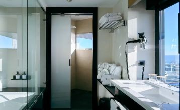 Das Hotel Barcelona Princess ragt inmitten der Hochhäuser Barcelonas nahe der Küste empor, unter einem teilweise bewölkten Himmel, unter dem sich Straßen, Autos und Bäume erstrecken – ein idealer Ort für die sportliche Vorbereitung.