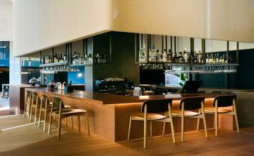 Das Hotel Barcelona Princess ragt inmitten der Hochhäuser Barcelonas nahe der Küste empor, unter einem teilweise bewölkten Himmel, unter dem sich Straßen, Autos und Bäume erstrecken – ein idealer Ort für die sportliche Vorbereitung.