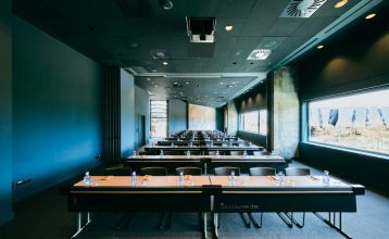 Das Hotel Barcelona Princess ragt inmitten der Hochhäuser Barcelonas nahe der Küste empor, unter einem teilweise bewölkten Himmel, unter dem sich Straßen, Autos und Bäume erstrecken – ein idealer Ort für die sportliche Vorbereitung.