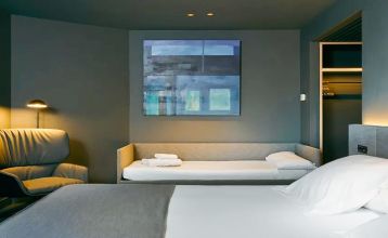 Das Hotel Barcelona Princess ragt inmitten der Hochhäuser Barcelonas nahe der Küste empor, unter einem teilweise bewölkten Himmel, unter dem sich Straßen, Autos und Bäume erstrecken – ein idealer Ort für die sportliche Vorbereitung.