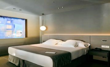 Das Hotel Barcelona Princess ragt inmitten der Hochhäuser Barcelonas nahe der Küste empor, unter einem teilweise bewölkten Himmel, unter dem sich Straßen, Autos und Bäume erstrecken – ein idealer Ort für die sportliche Vorbereitung.