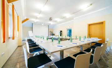 Das Hotel-Restaurant Schachenwald ist ein leuchtend gelbes, zweistöckiges Gebäude mit rotem Ziegeldach vor blauem Himmel – ideal für Trainingslager –, mit Topfpflanzen am Eingang und Autos, die auf der gepflasterten Zufahrt geparkt sind.
