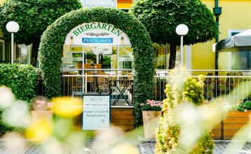Das Hotel-Restaurant Schachenwald ist ein leuchtend gelbes, zweistöckiges Gebäude mit rotem Ziegeldach vor blauem Himmel – ideal für Trainingslager –, mit Topfpflanzen am Eingang und Autos, die auf der gepflasterten Zufahrt geparkt sind.