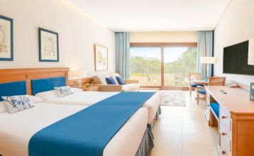 Das Hotel SH Villa Gadea* ist ein Resort an der Küste mit Meerblick, einem großen weißen Gebäude, einem Pool, Palmen und grünen Rasenflächen – ideal für Fußballmannschaften während ihres Trainingslagers in Altea unter strahlend blauem Himmel.
