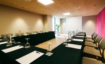 Ein Innenhof mit Palmen und Sitzgelegenheiten im Freien ist von modernen weißen Gebäuden umgeben, mit einem Hotel Zenit Sevilla-Schild - ideal für Fußball-Sportgruppen - und einem großen Gebäude mit der Aufschrift GOOD NIGHT auf dem Dach.