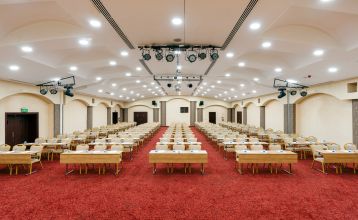 Luftaufnahme des Hotels Limak Arcadia mit Pools, Gärten, Sportplätzen und Strandkabinen - ideal für das Fußballtrainingslager Türkei - inmitten von Palmen und Bergen unter einem klaren Himmel.
