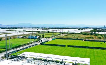 Luftaufnahme des Hotels Limak Arcadia mit Pools, Gärten, Sportplätzen und Strandkabinen - ideal für das Fußballtrainingslager Türkei - inmitten von Palmen und Bergen unter einem klaren Himmel.