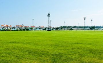 Luftaufnahme des Hotels Limak Arcadia mit Pools, Gärten, Sportplätzen und Strandkabinen - ideal für das Fußballtrainingslager Türkei - inmitten von Palmen und Bergen unter einem klaren Himmel.