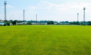 Luftaufnahme des Hotels Limak Arcadia mit Pools, Gärten, Sportplätzen und Strandkabinen - ideal für das Fußballtrainingslager Türkei - inmitten von Palmen und Bergen unter einem klaren Himmel.