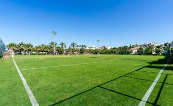 Luftaufnahme des Hotels Limak Arcadia mit Pools, Gärten, Sportplätzen und Strandkabinen - ideal für das Fußballtrainingslager Türkei - inmitten von Palmen und Bergen unter einem klaren Himmel.