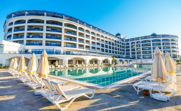 Das Side Moon Palace ist ein modernes Hotel mit mehreren Etagen und Balkonen, von denen aus man den Blick auf einen großzügigen Außenpool genießen kann, der von Reihen weißer Liegestühle und geschlossenen Sonnenschirmen gesäumt ist.