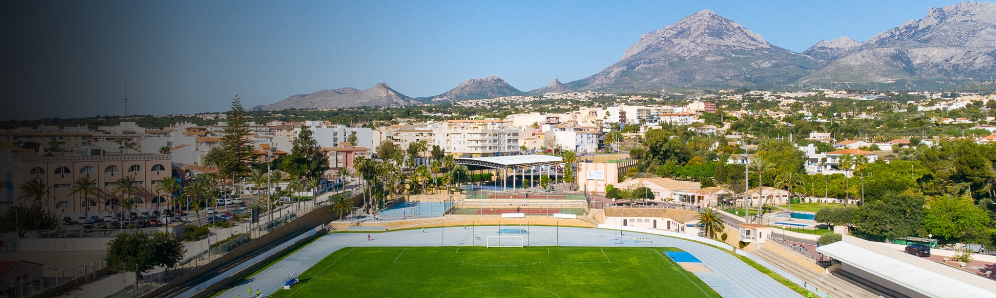 Ein gepflegtes Stadion mit Laufbahn, grüner Rasenfläche und Bergpanorama im Hintergrund.