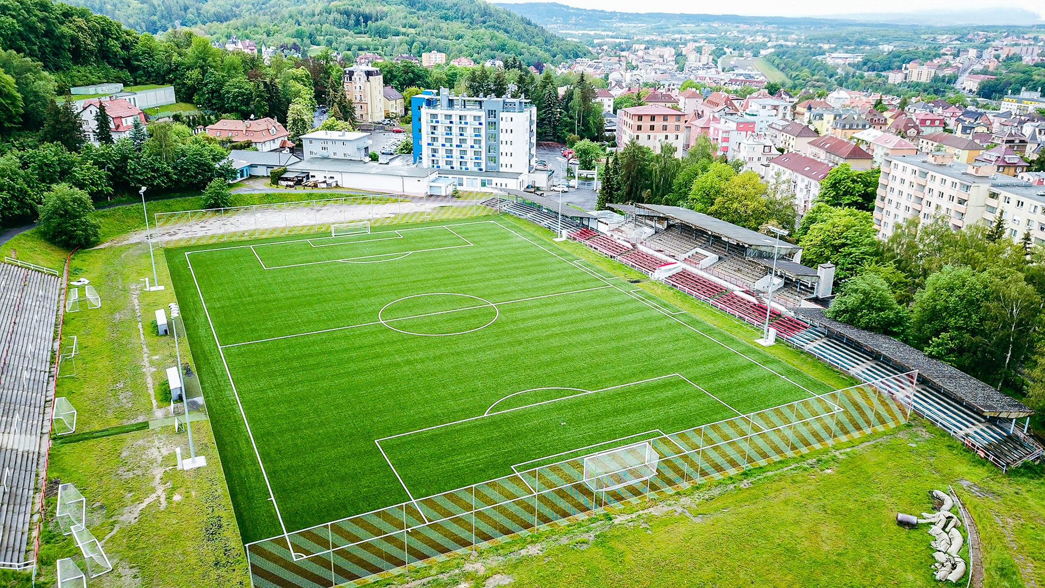  Fußballstadion mit Tribünen, umgeben von einer hügeligen Stadtlandschaft mit vielen Bäumen.
