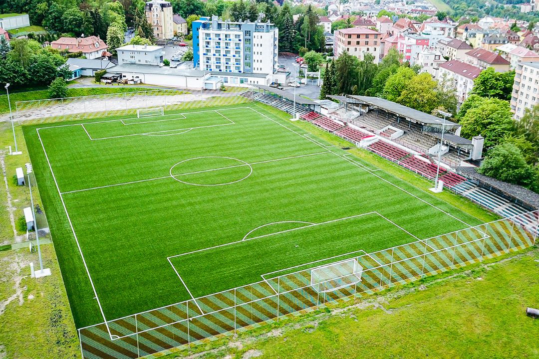  Fu&szlig;ballstadion mit Trib&uuml;nen, umgeben von einer h&uuml;geligen Stadtlandschaft mit vielen B&auml;umen.