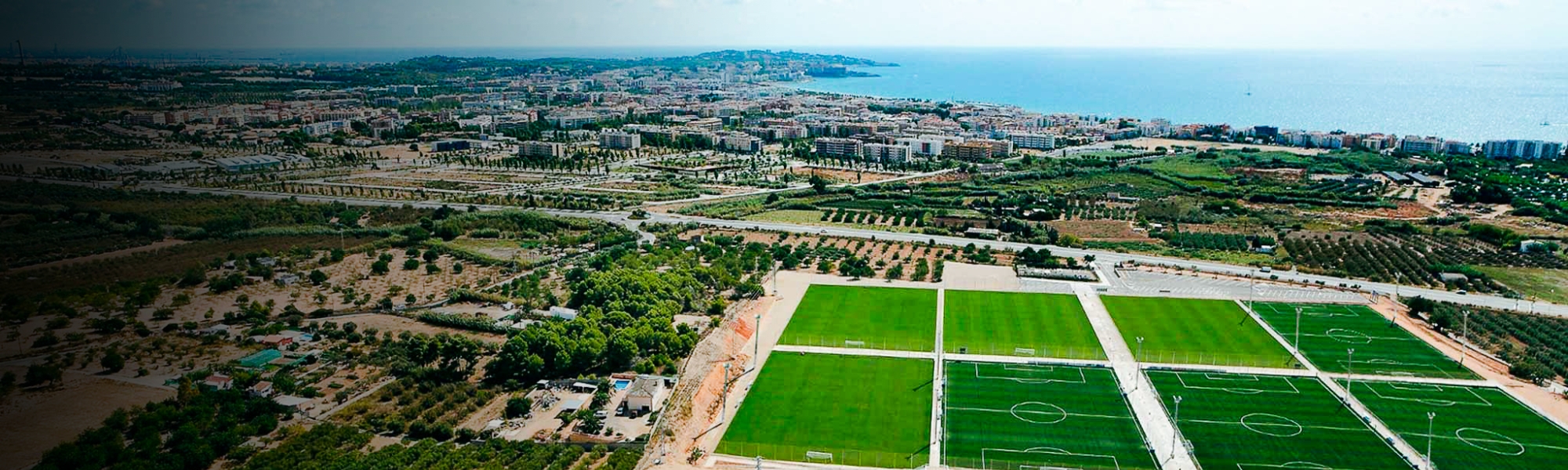 Eine moderne Sportanlage mit mehreren Fußballfeldern, Küstenaussicht und urbaner Umgebung.
