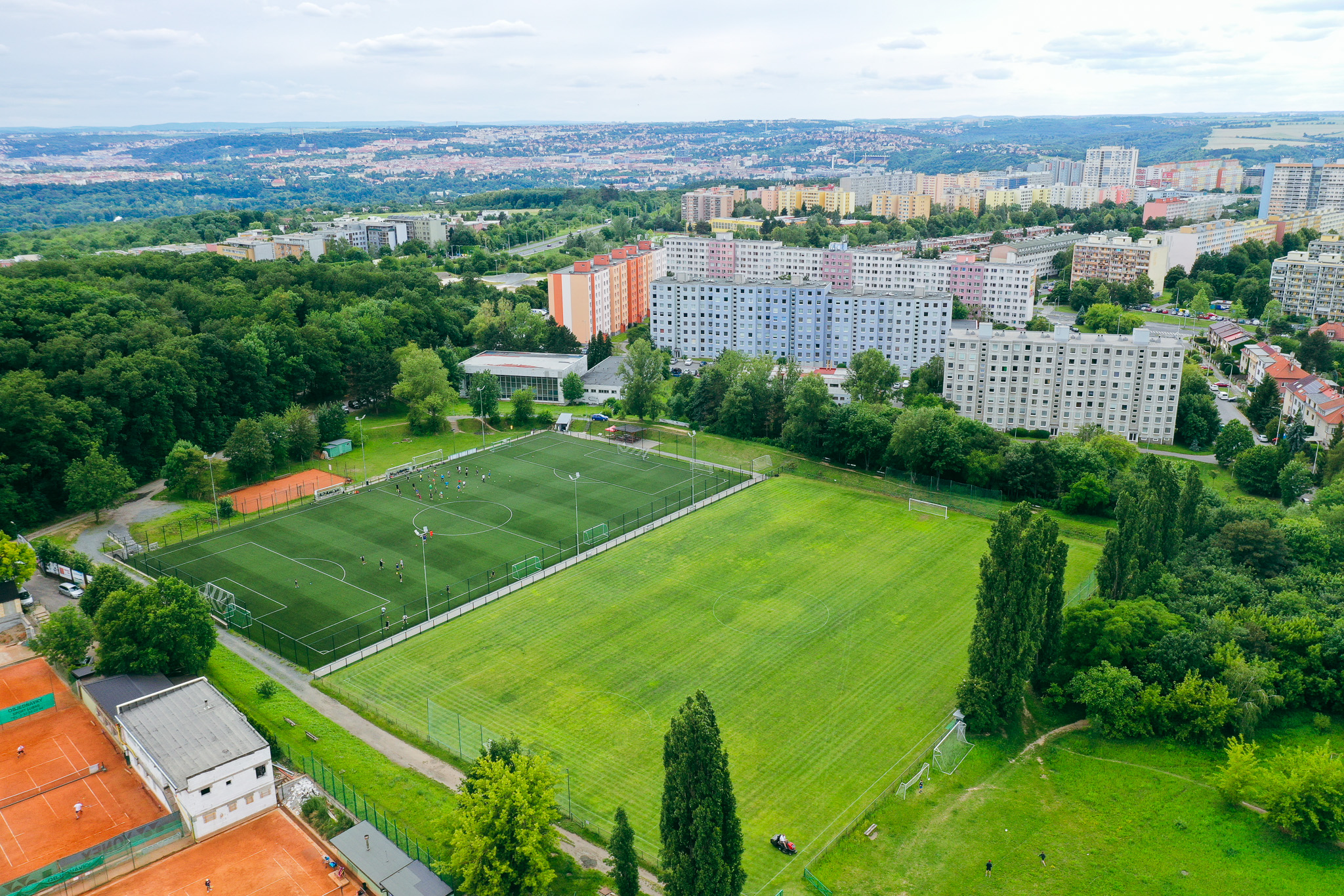 Fußballplatz inmitten einer grünen Landschaft mit Blick auf eine Stadt mit vielen Hochhäusern.