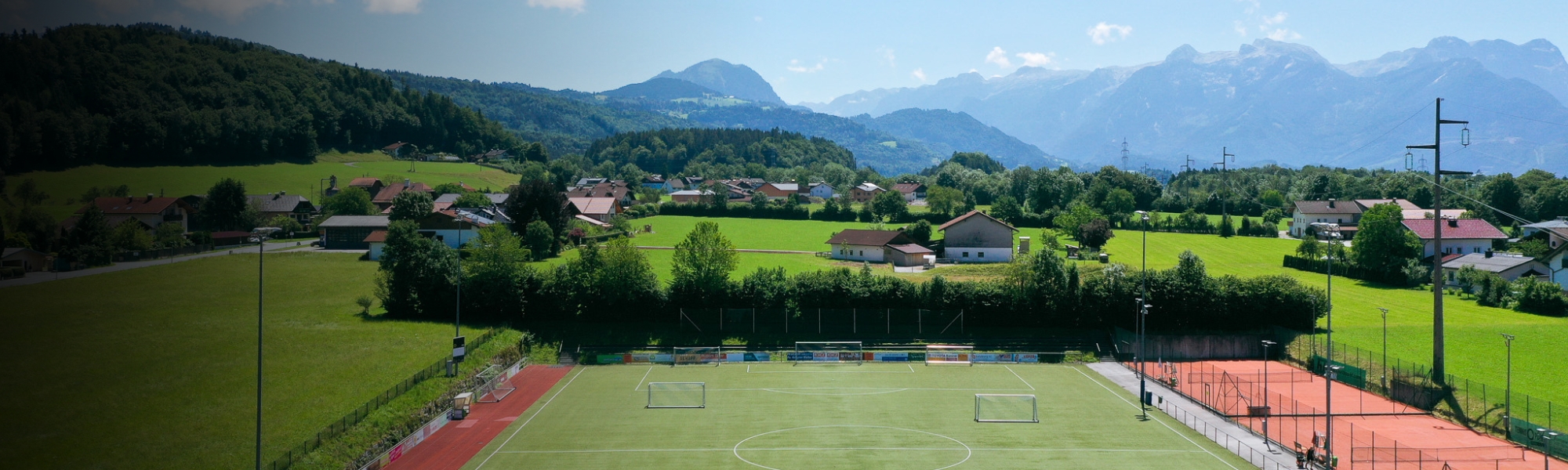 Fußballtrainingsanlage in Salzburg mit Kunstrasenplatz, roten Laufbahnen und Tennisplätzen, eingebettet in eine idyllische Alpenlandschaft.